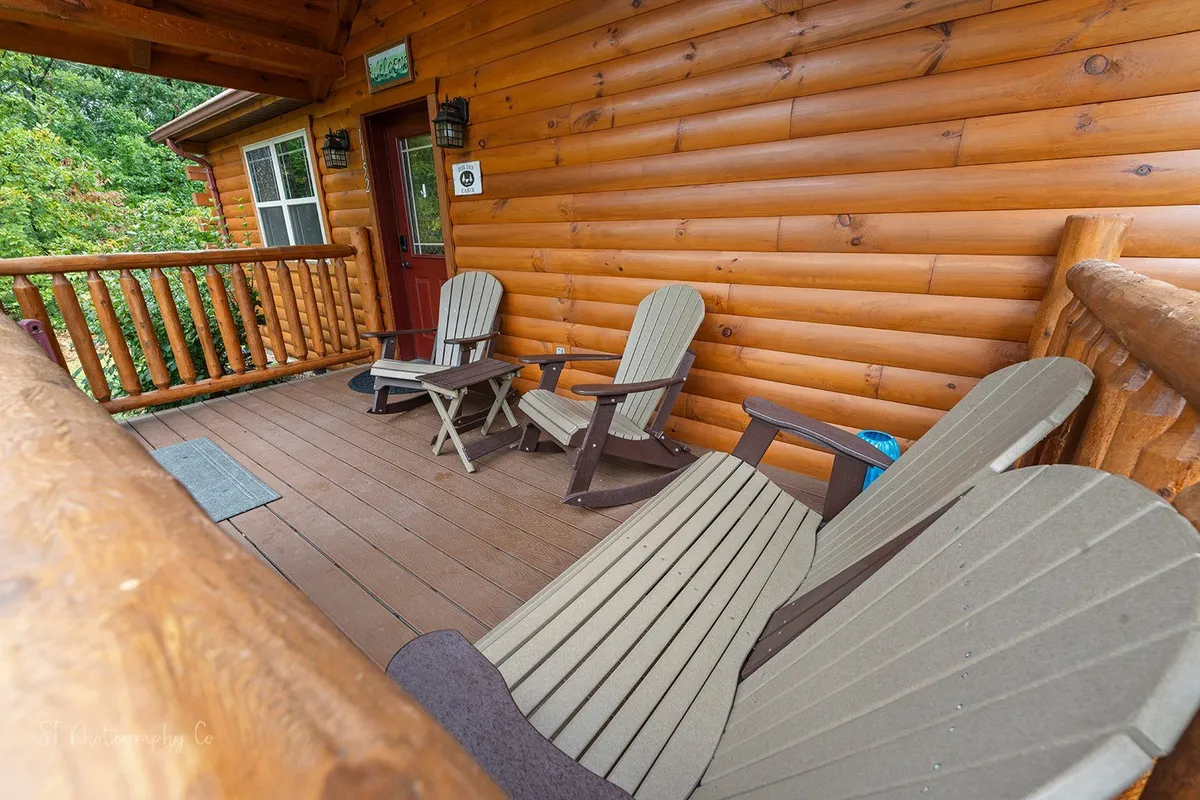 This image captures the inviting porch with classic wooden log walls and rocking chairs, set against a backdrop of lush greenery. The entrance area radiates a welcoming atmosphere for coming and going between the cabin and local attractions.