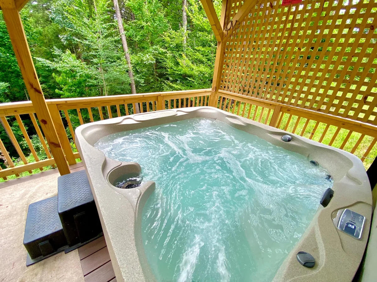 This exterior image features a private hot tub set within a wooden structure, surrounded by vibrant greenery. The tranquil setup invites guests to unwind outdoors, whether by day or under the stars, and hints at the social possibilities the hot tub offers.