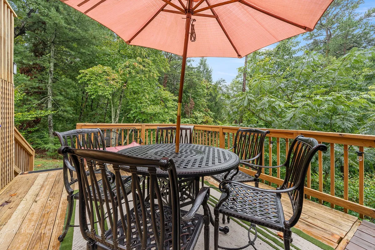An exterior dining area featuring a table with chairs under a pink umbrella, nestled in a peaceful green setting. This space is ideal for casual gatherings, outdoor meals, or sharing stories after a night out.