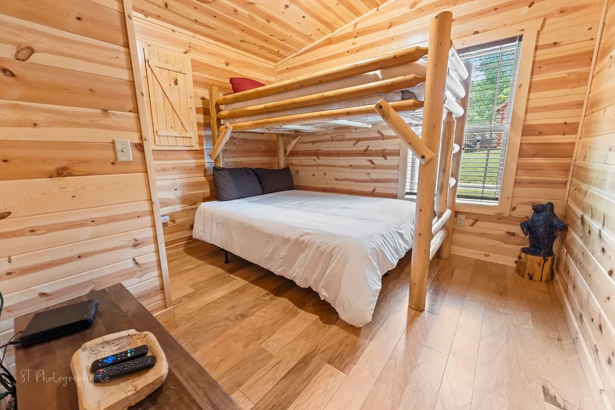 A cheerful bunk bedroom with a twin over queen bunk bed, wooden flooring, and a window allowing for ample natural light. The space feels inviting and playful, ideal for kids or friends sharing stories and creating lasting memories.