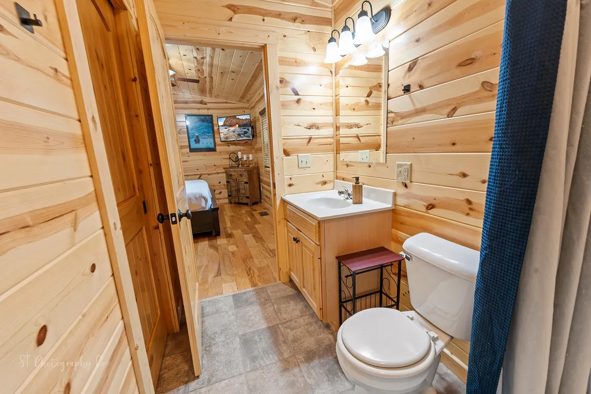 A bathroom with rustic wooden walls, a vanity with a sink, soft lighting, and thoughtful bathroom accessories. The ambiance is both comfortable and tranquil, inviting guests to refresh and unwind.