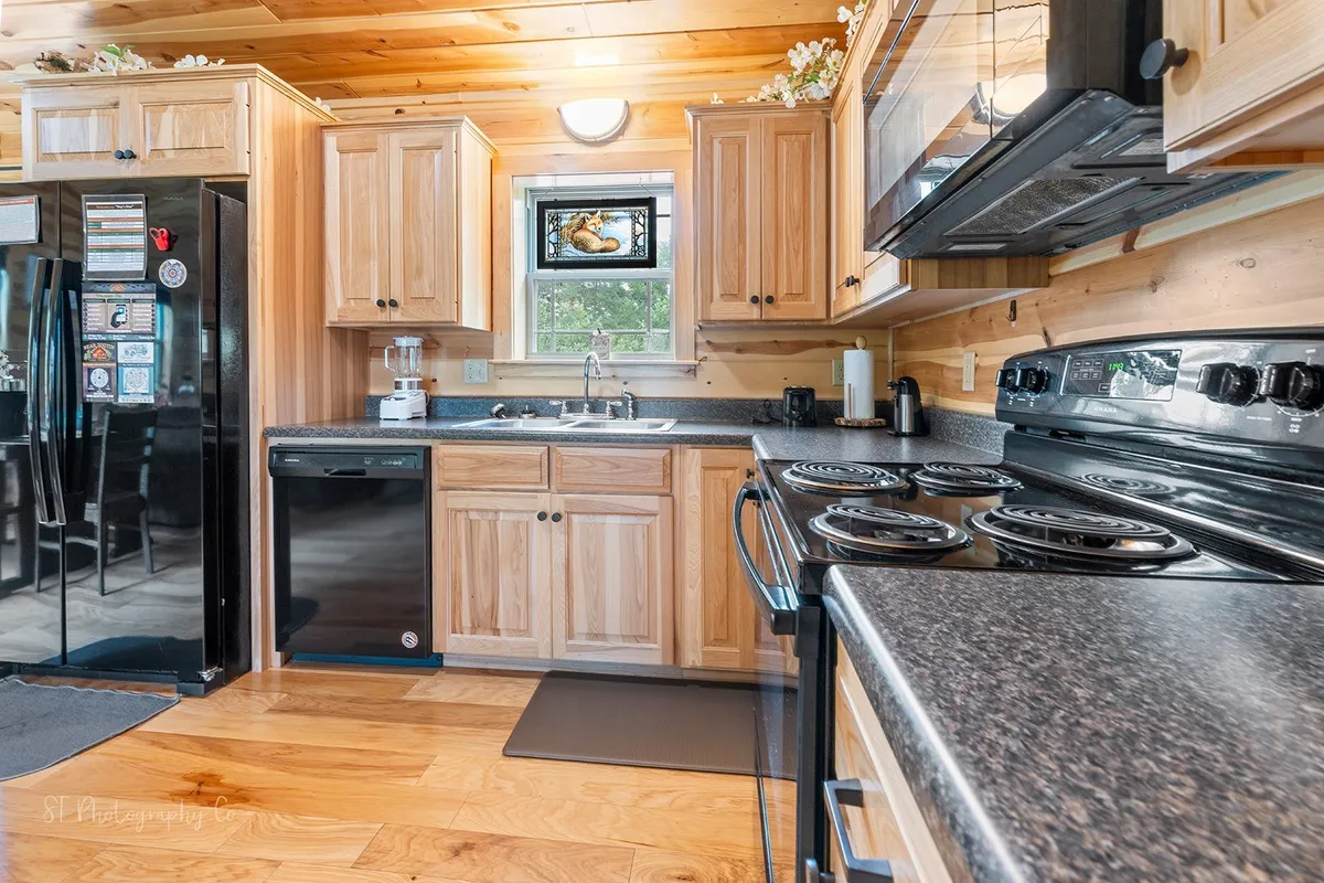 A warmly lit kitchen featuring stainless steel appliances, wooden cabinetry, a black countertop, and a window with decorative glass. The kitchen appears well-equipped and spacious, with ample counter space for meal preparation. The ambiance suggests a welcoming space ideal for cooking and gathering.