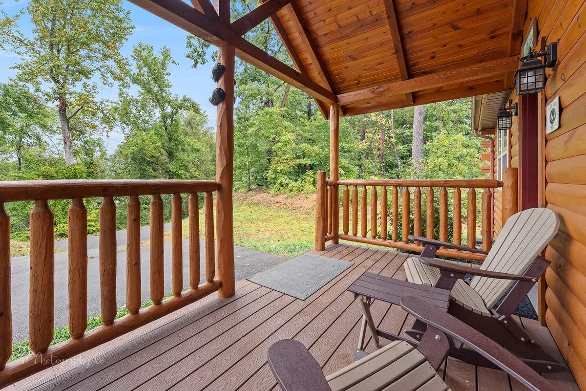 This image features a spacious wooden porch lined with rocking chairs, surrounded by lush greenery. The sturdy wooden railing and ample seating invite guests to relax and take in the sights and sounds of the natural setting.